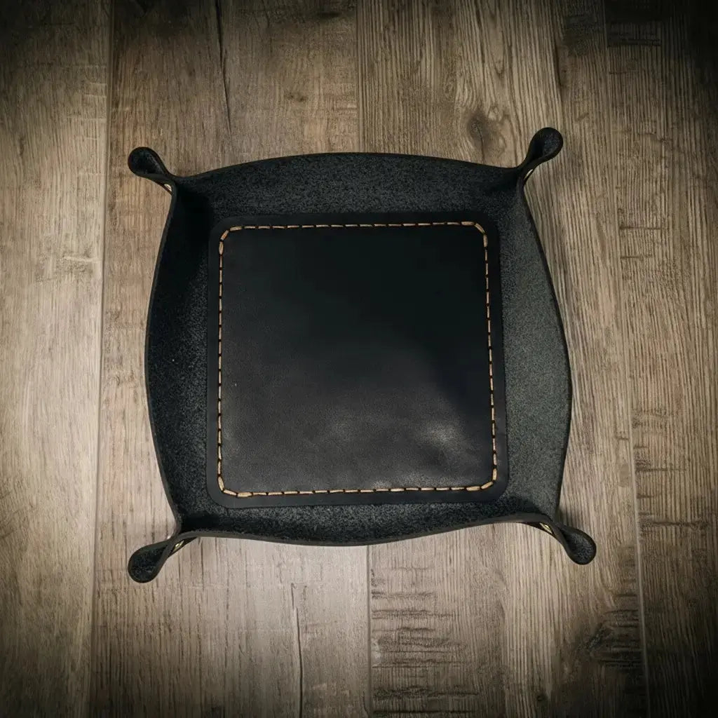 Black leather valet tray with tan stitching on a wooden background.