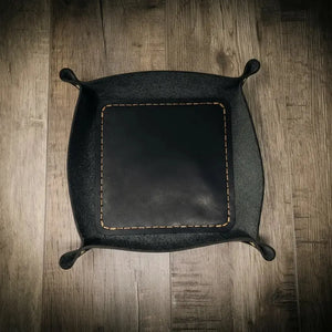 Black leather valet tray with tan stitching on a wooden background.