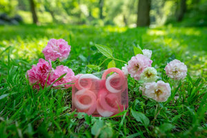 Pink and white spiral soap slice in clear packaging surrounded by grass and pink roses.