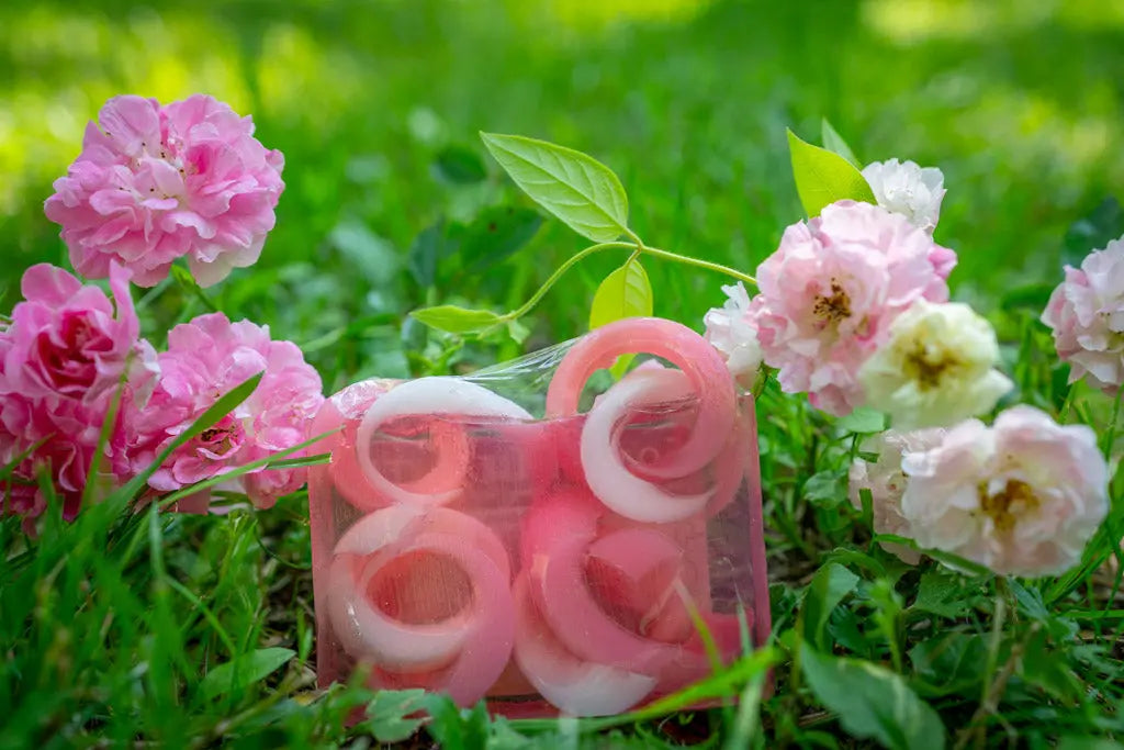 Pink and white swirl soap slices surrounded by pink roses and green grass.