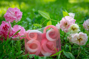 Pink and white swirl soap slices surrounded by pink roses and green grass.