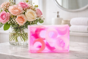 Pink rose soap slice with ring-shaped inclusions on a marble surface.
