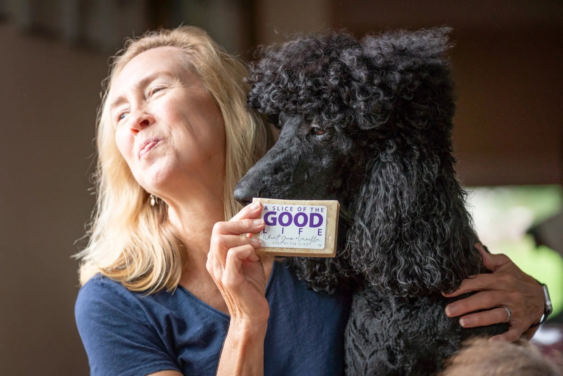 Woman holding a bar of Wheat Germ & Vanilla soap next to a black poodle.