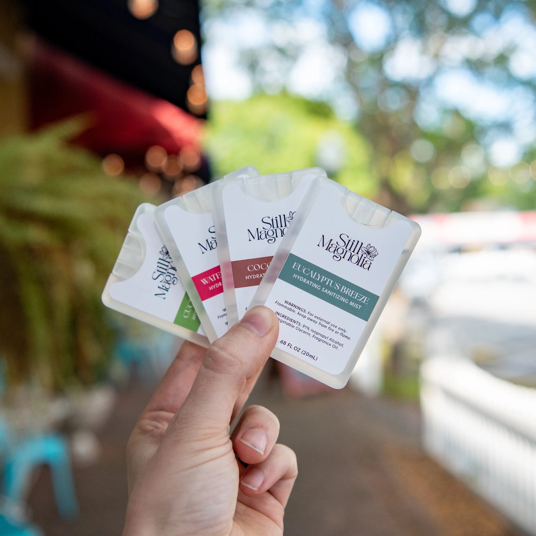 Hand holding four pocket-sized Still Magnolia sanitizing mist bottles