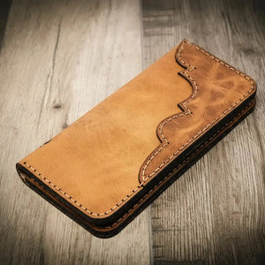 Brown leather Western long bifold wallet with decorative stitching on a wood surface.