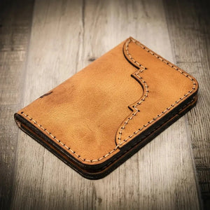 Brown leather Western vertical wallet with decorative stitching on a wooden background.