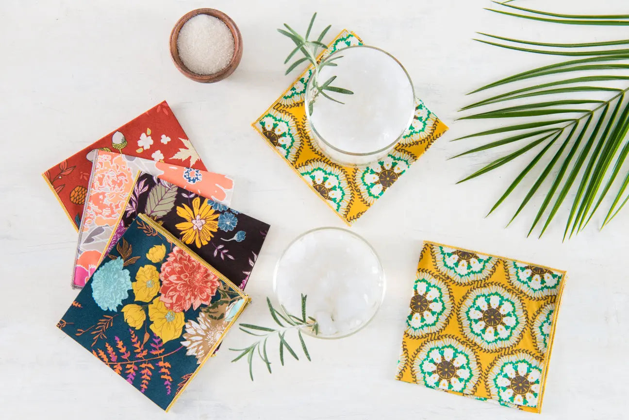Set of four square cloth napkins with a blue and floral pattern and yellow trim.