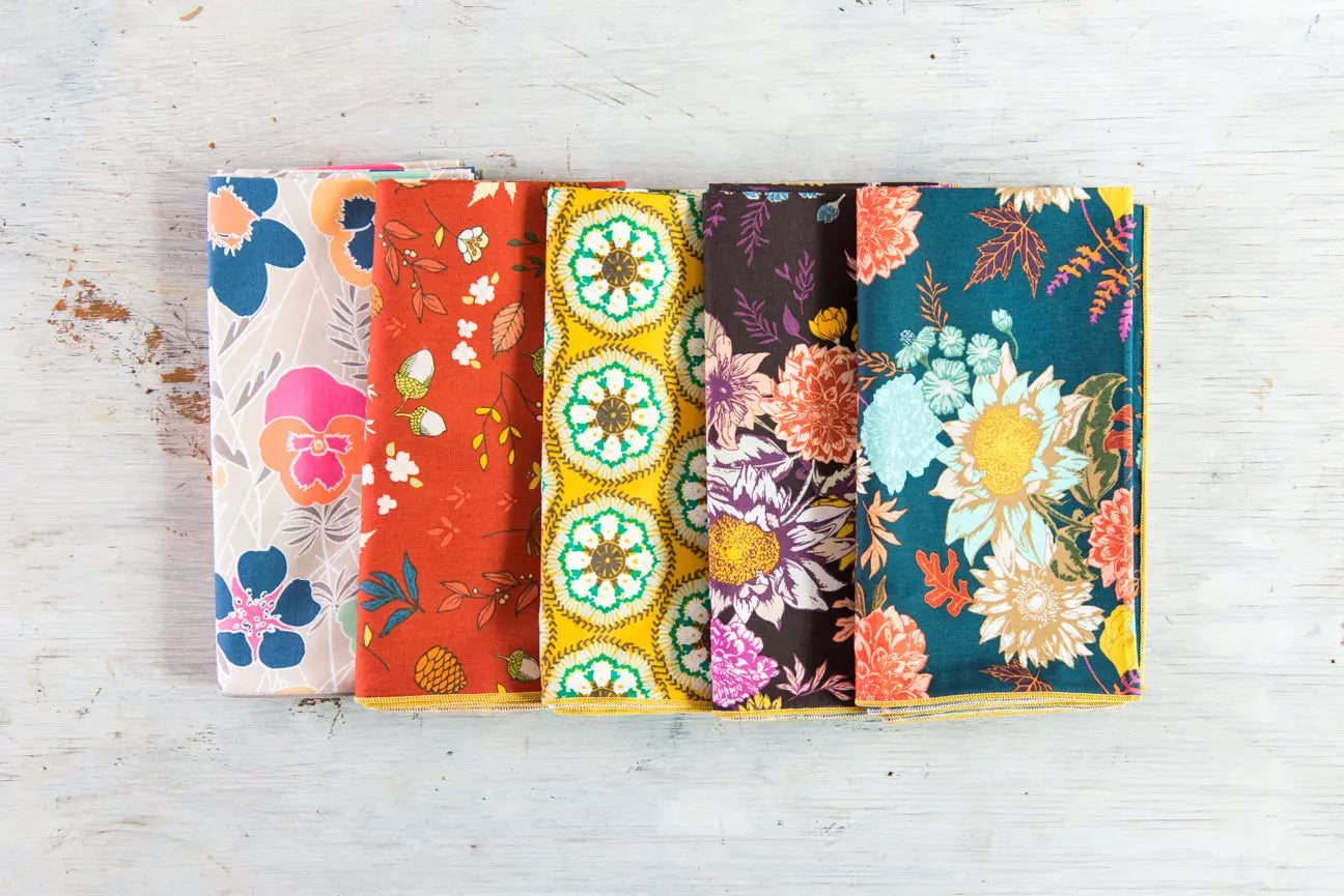Set of five cloth napkins with different floral and acorn patterns in various colors.