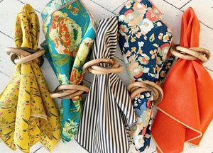 Wood bangles napkin rings holding colorful patterned fabrics and solid orange fabric.