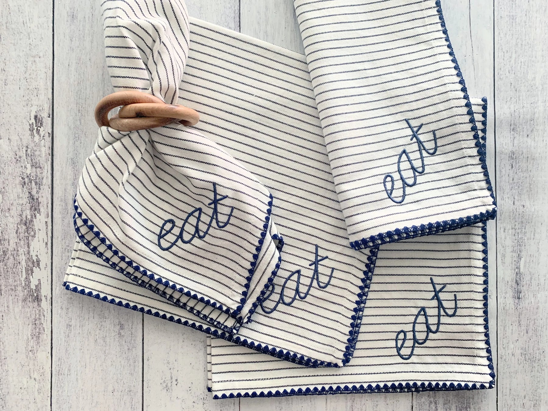 Striped fabric napkins with embroidered "EAT" and wooden bangle napkin rings.