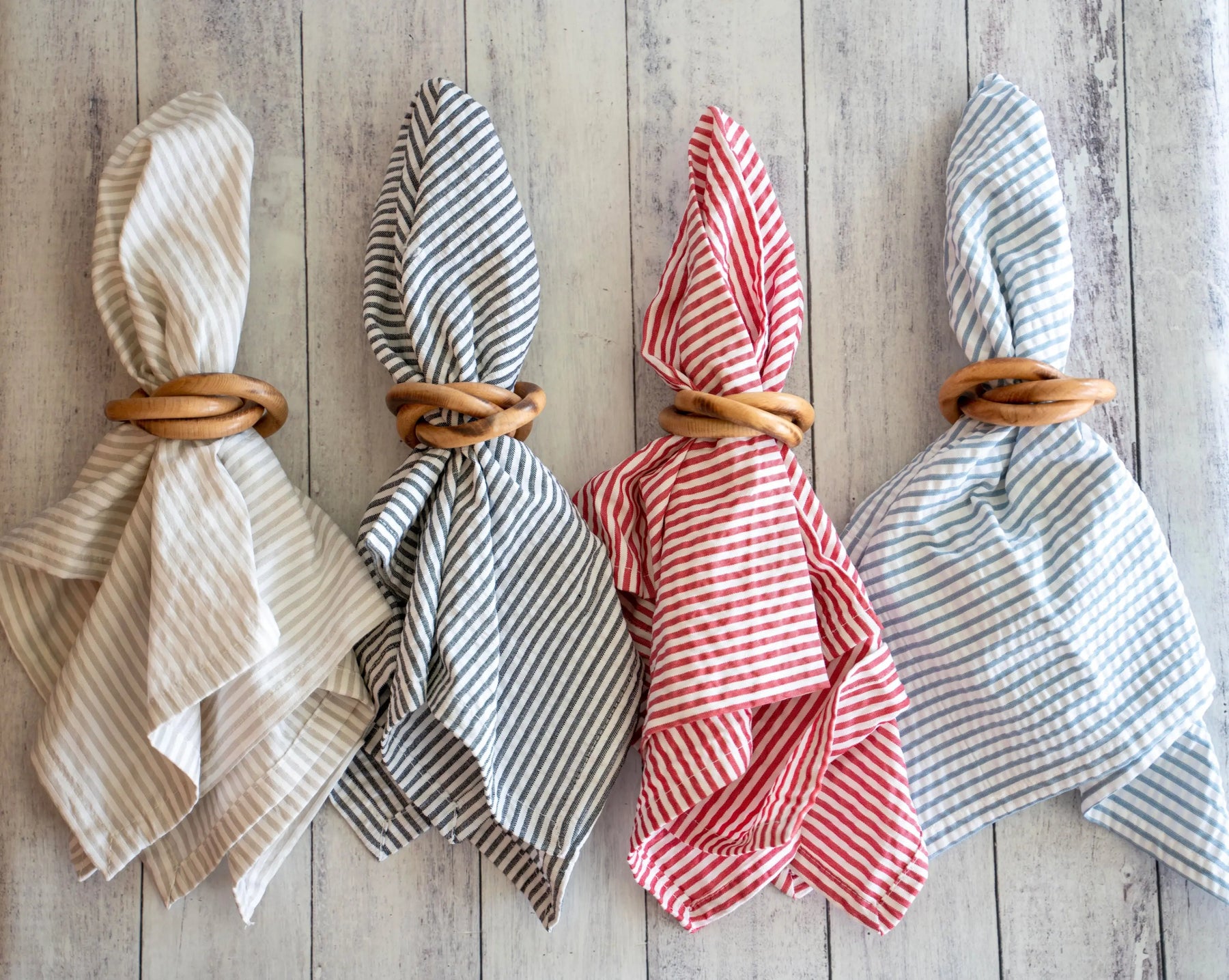 Set of four wooden napkin rings holding striped fabric napkins in beige, navy, red, and blue.
