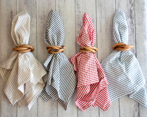 Set of four wooden napkin rings holding striped fabric napkins in beige, navy, red, and blue.