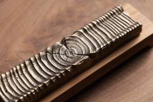 Handcrafted wood incense holder with bronze casting detail on a wooden surface.