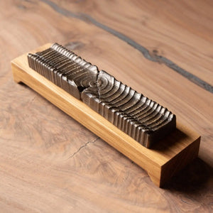 Wooden incense holder with bronze casting showing wood grain rings sitting on a light wood base on a wooden surface.