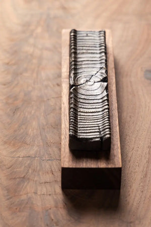 Wooden incense holder with bronze casting on a wood surface showing wood grain.