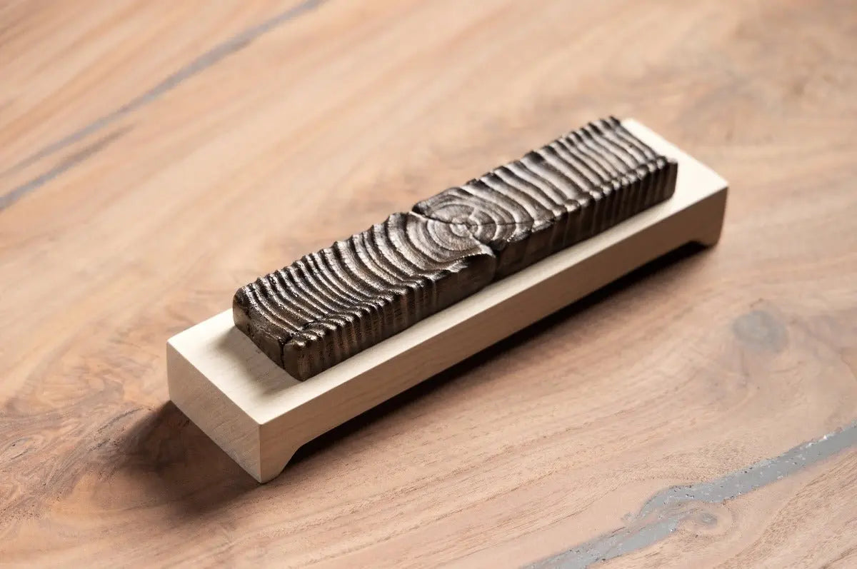 Wooden incense holder with bronze casting on a light wood base, displayed on a wood table.