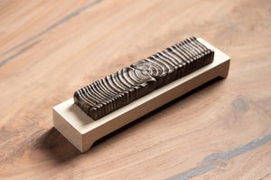 Wooden incense holder with bronze casting on a light wood base, displayed on a wood table.