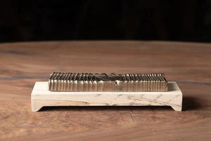 Wooden incense holder with bronze casting on a marble stand, seen on a wooden surface. The incense holder has a grooved top.