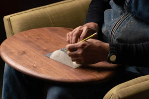 Walnut wooden lap desk with a person writing on paper using a pencil, sitting on a green chair, with a denim jacket.