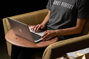 Walnut wooden lap desk with laptop on upholstered chair, featuring a person's hands on the keyboard.