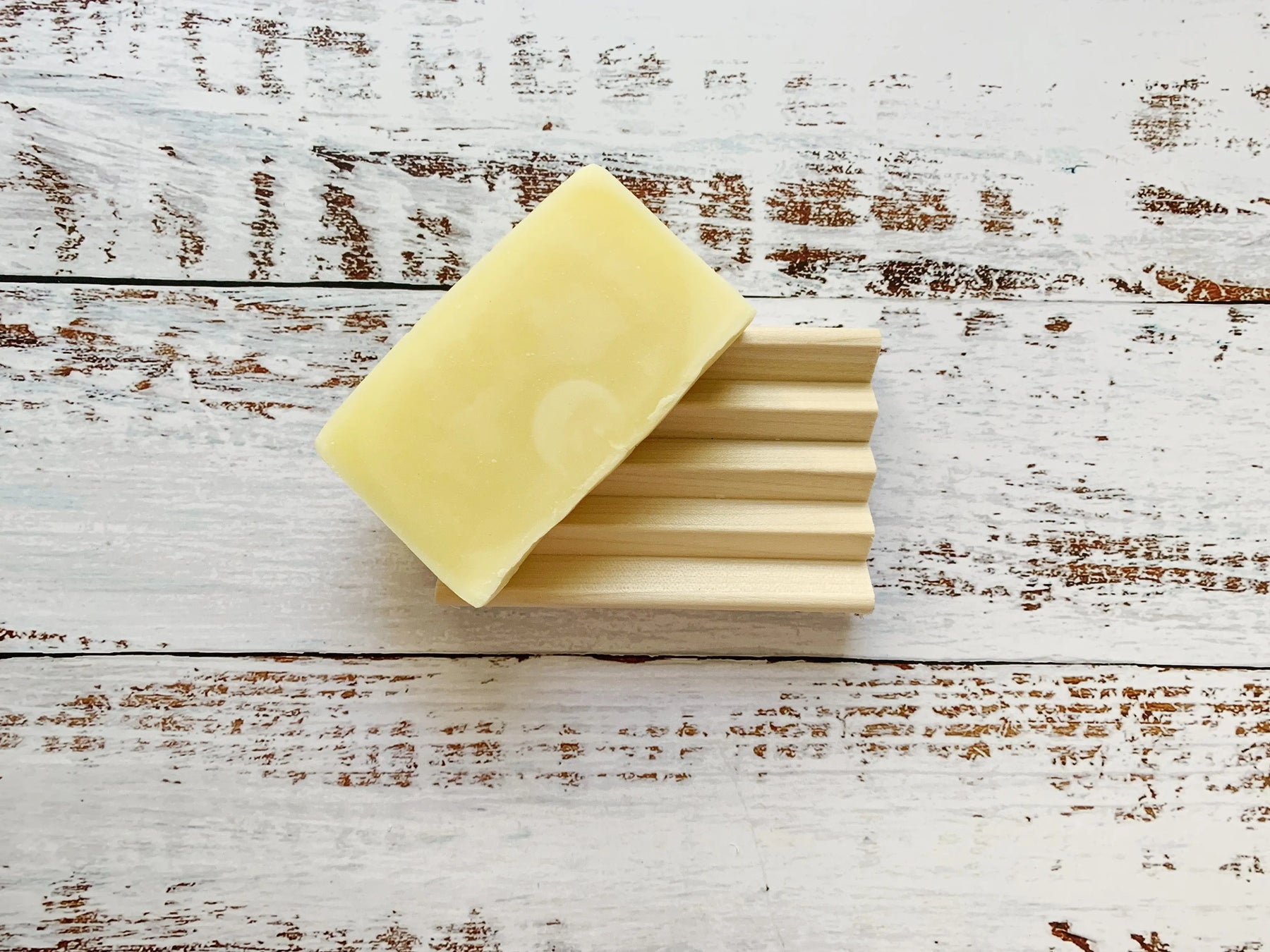 Natural wooden soap dish with deep grooves on a distressed white wooden background.