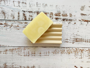 Natural wooden soap dish with deep grooves on a distressed white wooden background.