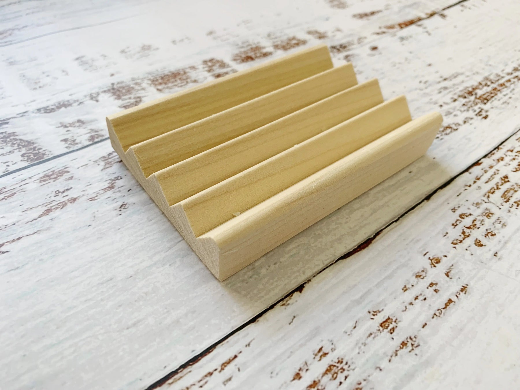 Natural wood soap dish with drainage grooves on a distressed white wood surface.