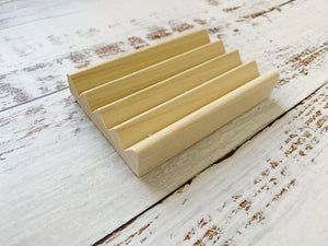 Natural wood soap dish with drainage grooves on a distressed white wood surface.