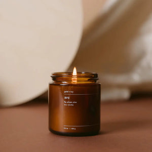 Amber jar soy candle with lit wick, labeled "arc gold + ivy" with scent notes fig, ginger, pine.