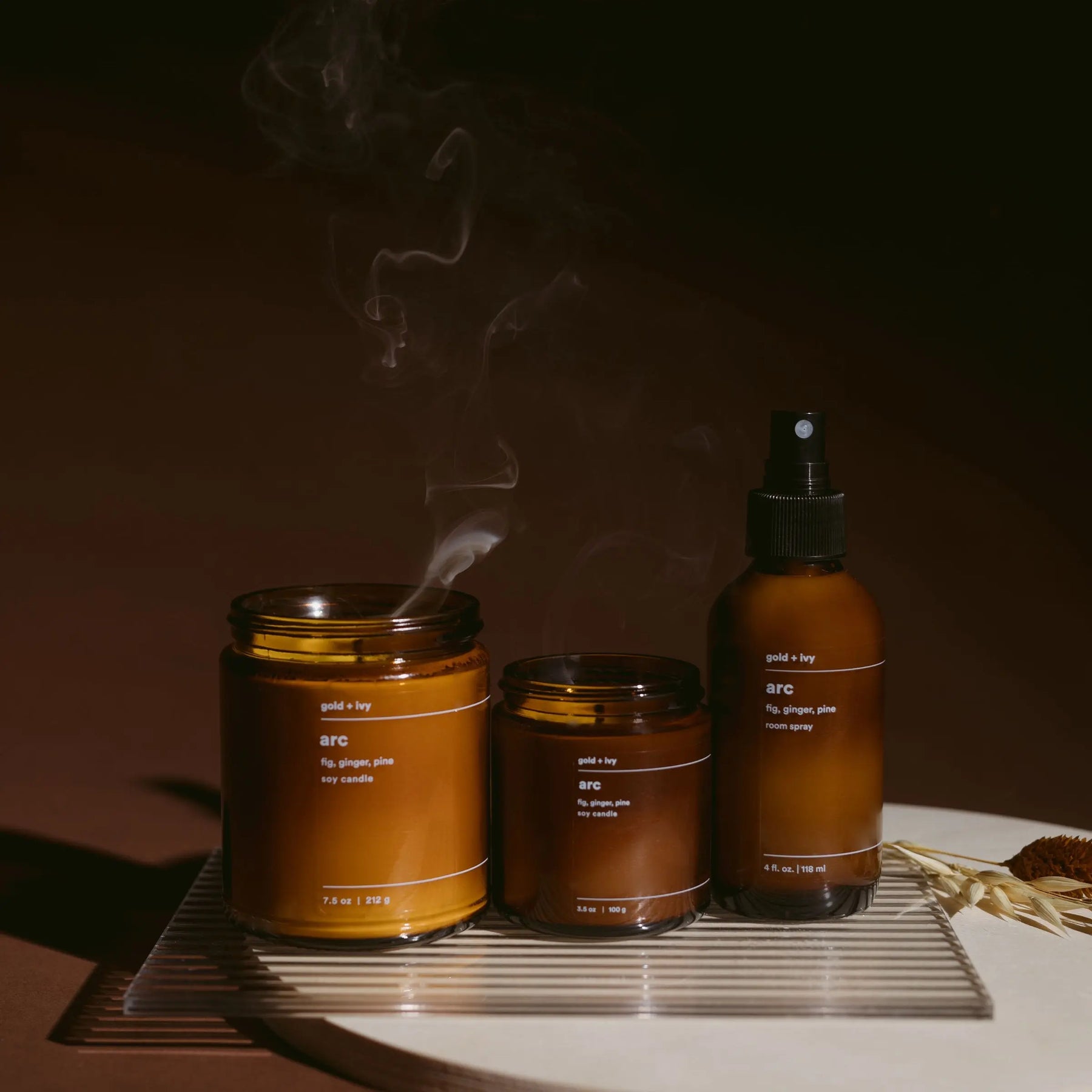 Three amber glass ARC "gold + ivy" scented products including two soy candles and one room spray.