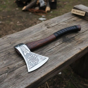 Damascus steel axe head with leather handle on rustic wood surface