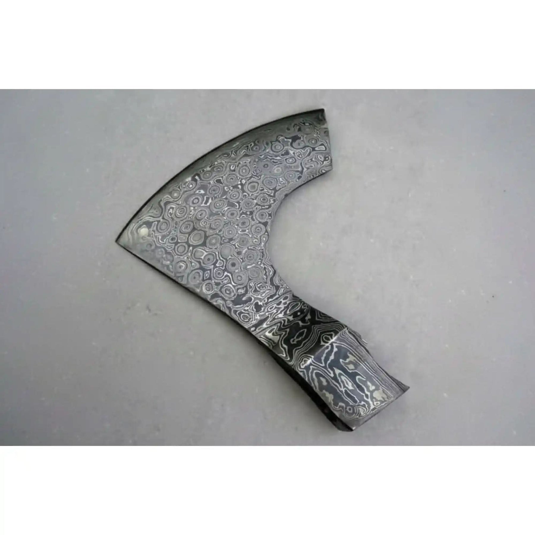 Damascus steel axe head with premium handle on rustic wood surface