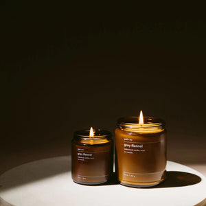 Two "gold + ivy" Grey Flannel scented soy candles in amber glass jars, one lit.