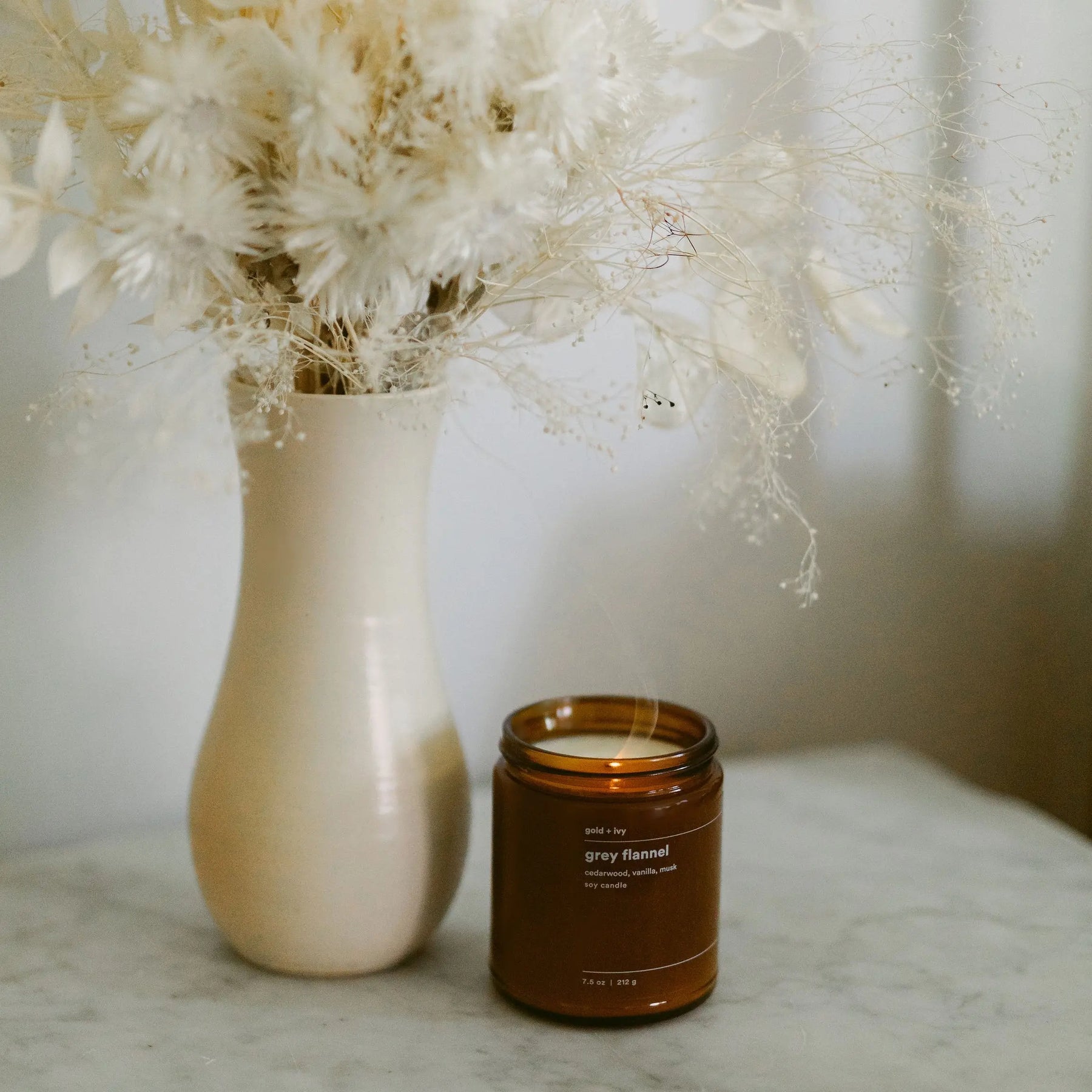 Gold + Ivy Grey Flannel soy candle in an amber glass jar with visible smoke.