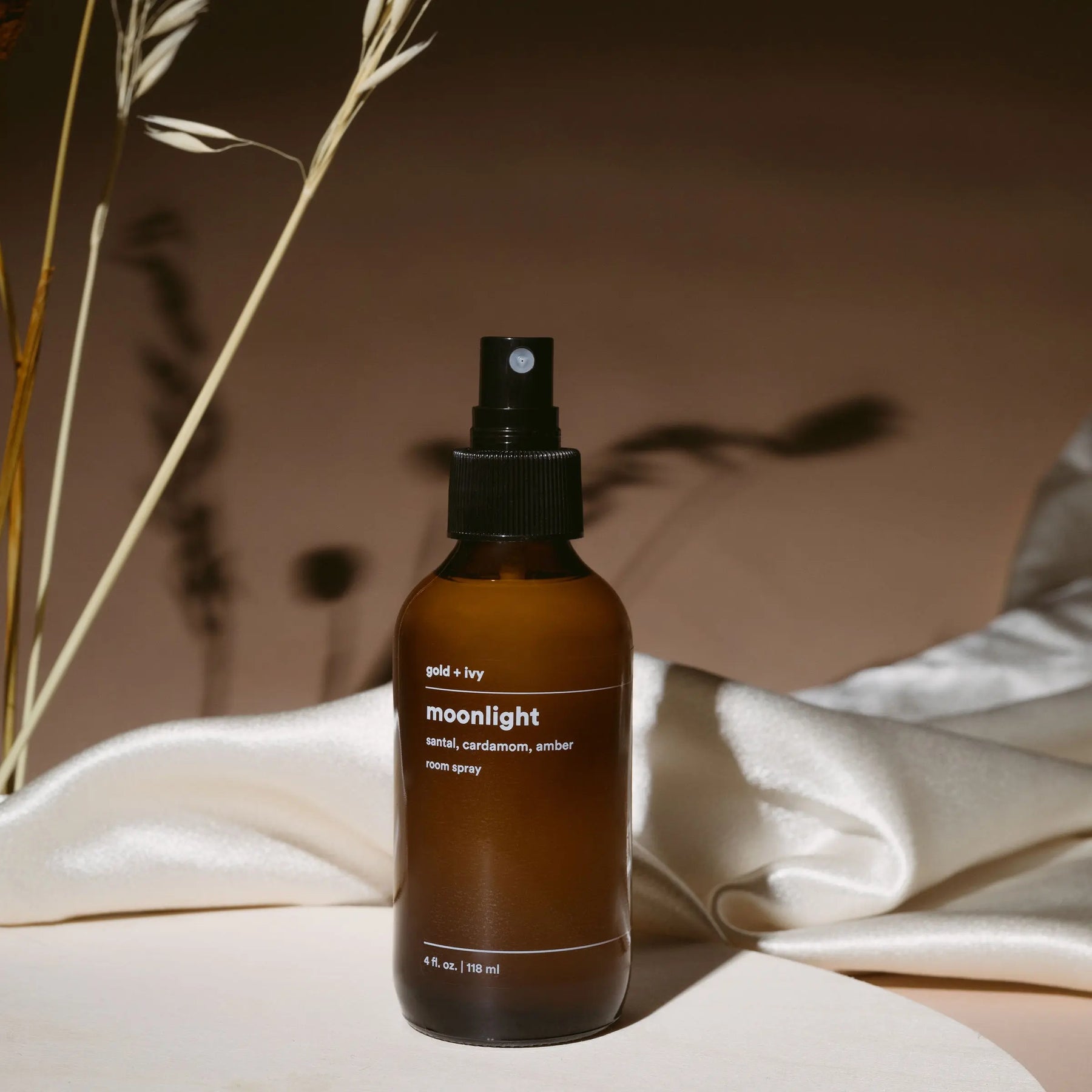 Gold + Ivy Moonlight room spray with sandalwood, cardamom, and amber notes in amber glass bottle.