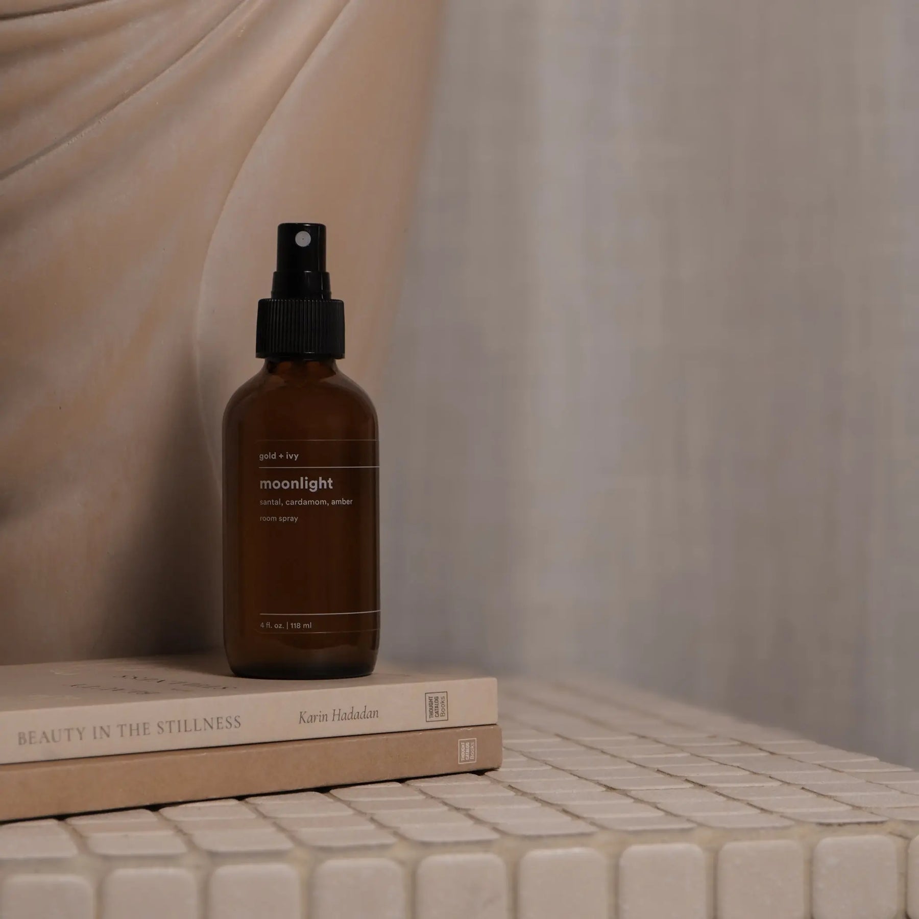 Gold + Ivy Moonlight room spray with sandalwood, cardamom, and amber scent on books.
