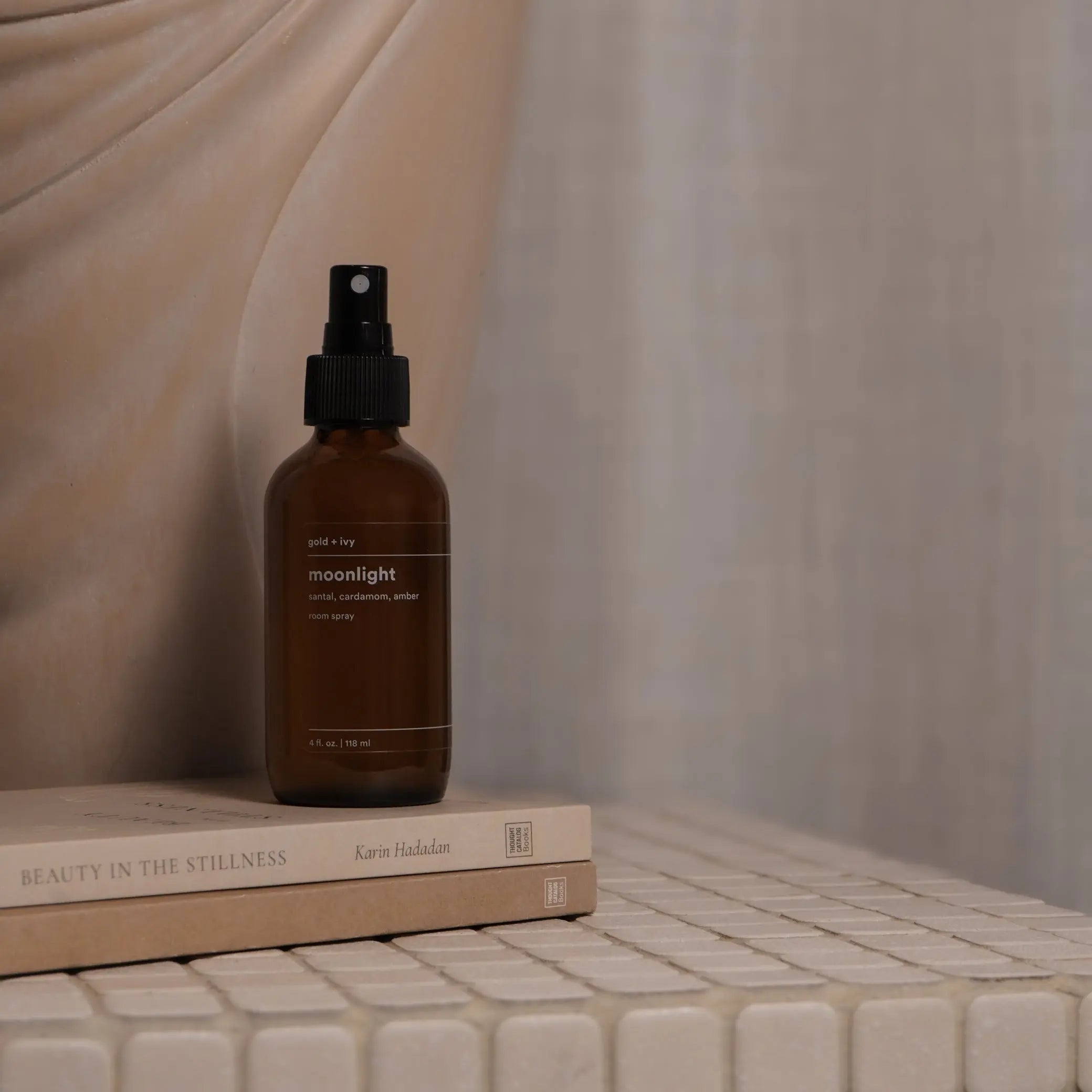 Gold + Ivy Moonlight room spray with sandalwood, cardamom, and amber scent on books.