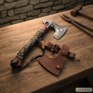 Damascus steel axe head with leather handle on rustic wood surface