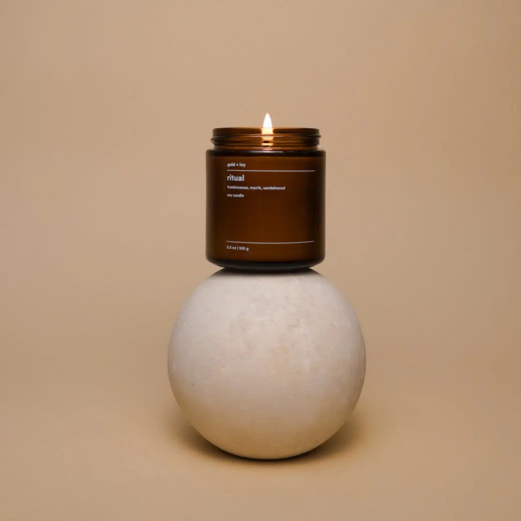 Amber glass ritual soy candle with a lit wick on a stone sphere.