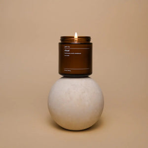 Amber glass ritual soy candle with a lit wick on a stone sphere.