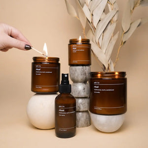 Brown glass Ritual soy candles and room spray with a lit match.