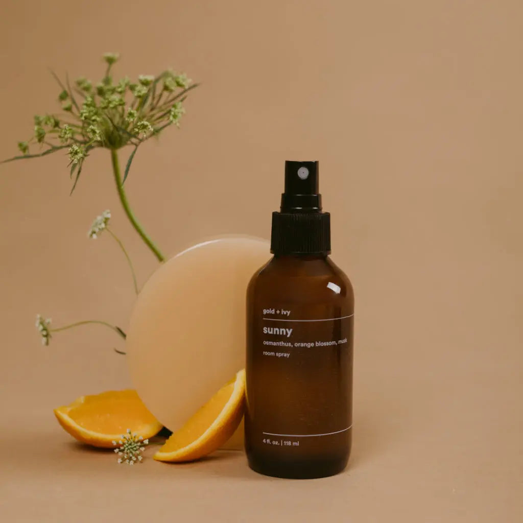Brown glass room spray bottle labeled Gold + Ivy Sunny, with orange slices and greenery.